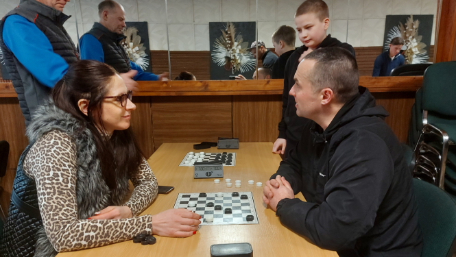 Sieviete pie galda spēlē dambreti ar vīrieti