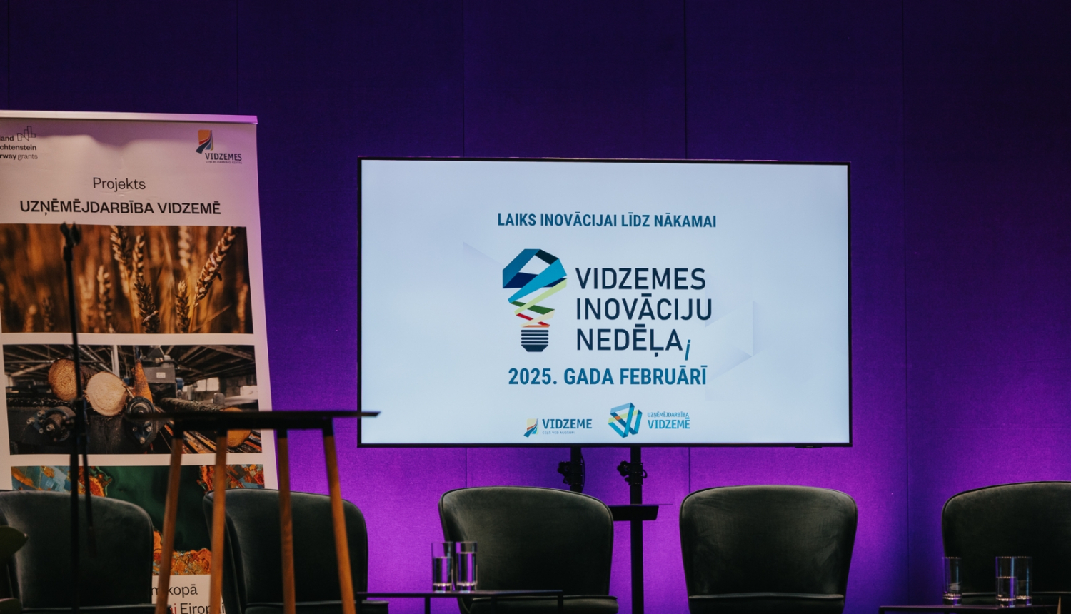 Konferences skatuve ar krēsliem un ekrānu ar Vidzemes Inovācijas nedēļas baneri