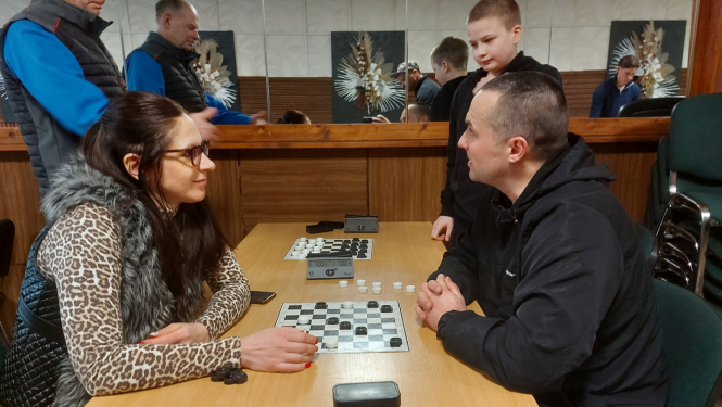 Sieviete pie galda spēlē dambreti ar vīrieti