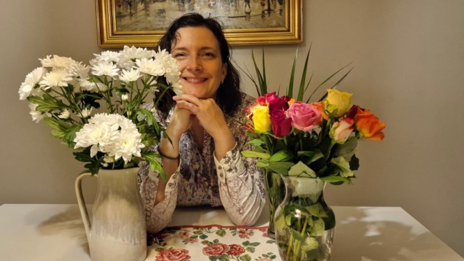 Smaidīga sieviete starp divām puķu vāzēm ar ziediem