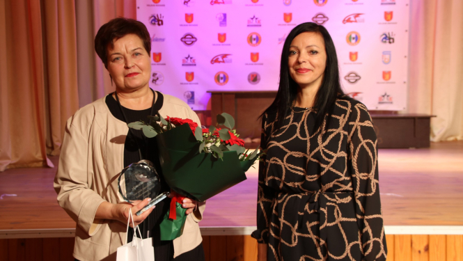 Divas sievietes ar turmšiem matiem, vienai rokās ziedu pušķi. 