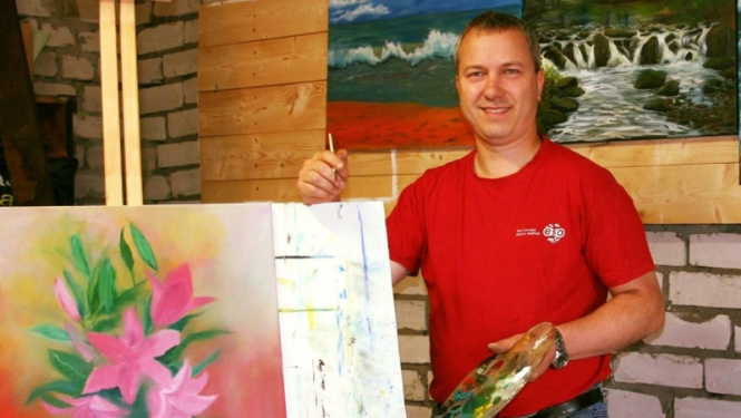 Vīrietis sarkanā kreklā pie molberta ar gleznu