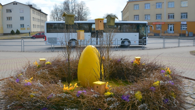 Lieldienu dekorācija - ola grozā priekšplānā un autobuss fonā
