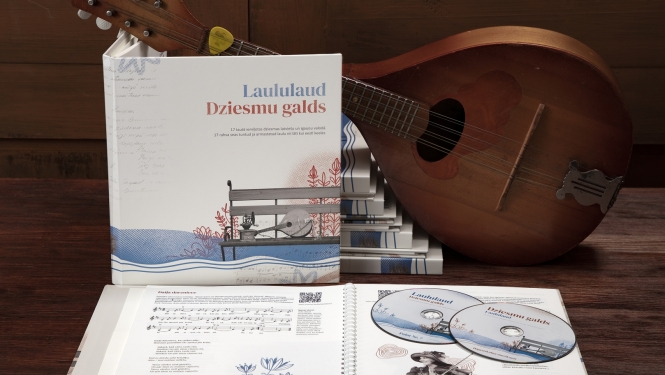 Uz galda uzlikta mandolīna ar "Dziesmu galds" grāmatu eksemplāriem