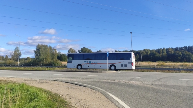 Balts autobuss uz ceļa, fonā zilas debesis