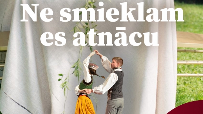 Galds ar baltu galdatu fonā, priekšplānā dejo puisis un meitene tradicionālā latviešu tautas terpā 