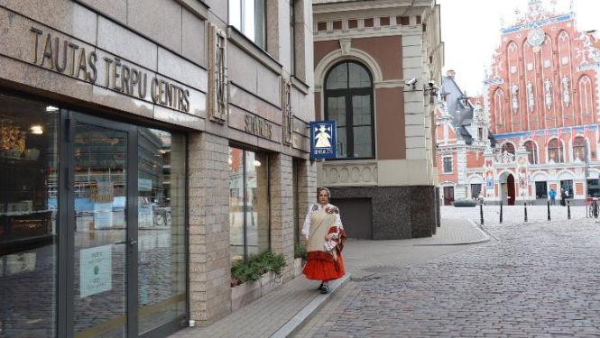 Sieviete latviešu tautas tērpā pie tautas tērpu centra ieejas