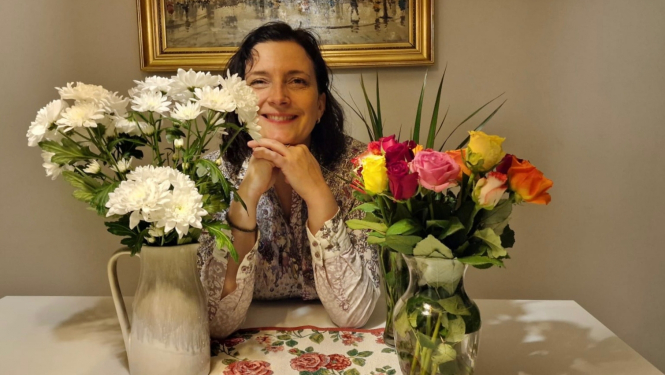 Smaidīga sieviete starp divām puķu vāzēm ar ziediem