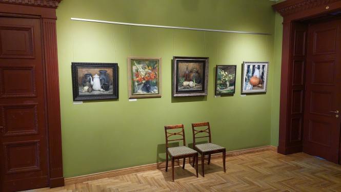 Gleznas uz zaļas sienas pie kuras ir divi krēsli