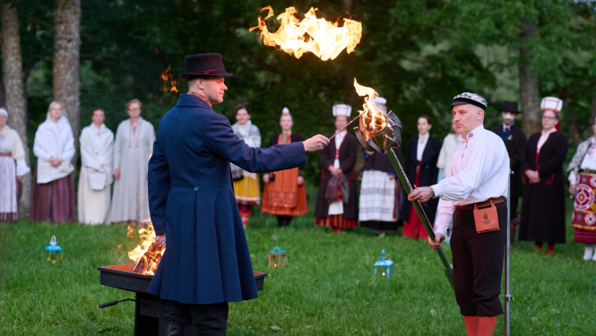 Vīrietis grenzā t;erpā aizdedzina metāla lāpu.