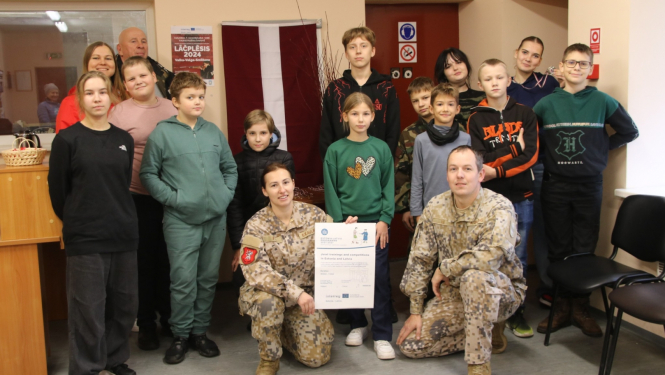 Sacensības dalībnieku un treneru kopbilde pie Latvijas karoga