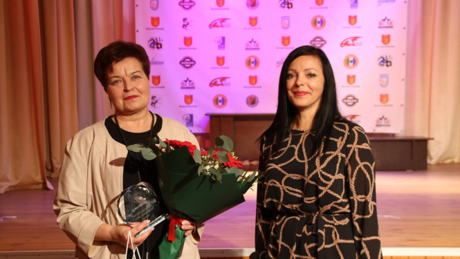 Divas sievietes ar turmšiem matiem, vienai rokās ziedu pušķi. 