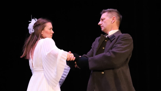 Sieviete baltā kleitā un vīrietis tumšā tērpā skatās viens uz otru uz tumša fona