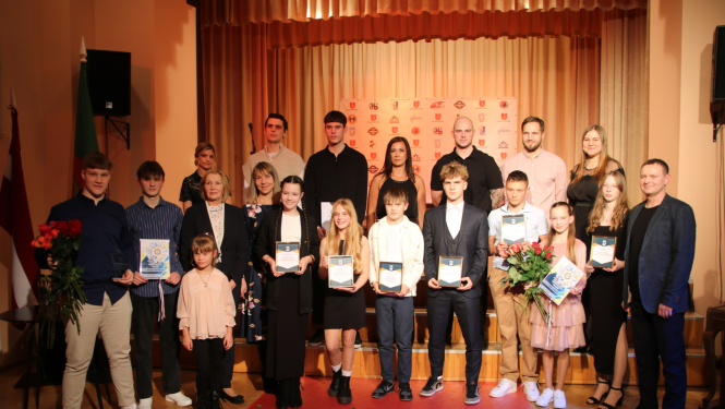 Kolektīva kopbilde ar skatuvi fonā