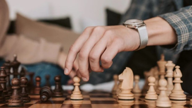 Cilvēka roka virs šaha galdiņa gatavojas veikt gājienu ar bandinieka kauiņu