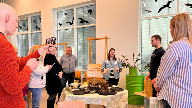 Cilvēki sastājušies ap galdu klausās stāstījumu par kompostiem