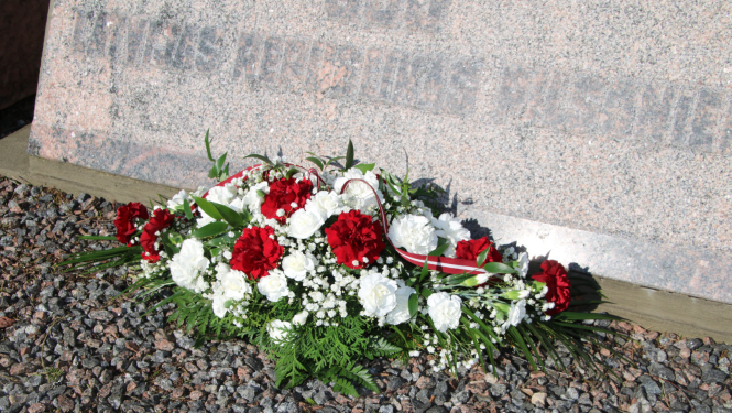 Sarkanu un baltu ziedu oāze pie piemiņas akmens