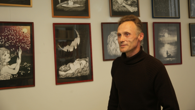 Vīrietis pusmūža vecumā pie sienas ar gleznām