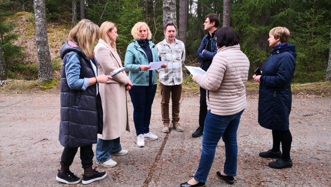 Speciālistu grupa 7 cuilvēki stāv pie meža teritorijas