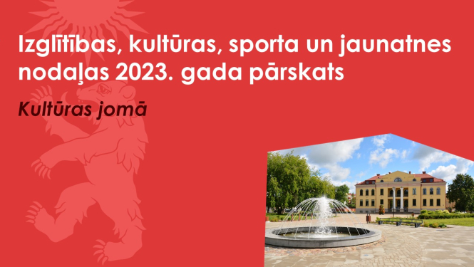 Sarkans baneris ar Valkas novada ģērboņa lāča siluetu un Valkas pilsētas kultūras nama ēka ar Lugažu laukuma strūklaku