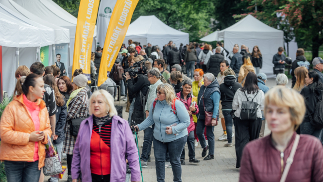 Pūlis ar cilvēkiem darba iespēju festivālā, malās baltas teltis un dzelteni vertikāli baneri