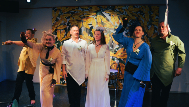 Seši cilvēki košos tērpos uz teātra skatuves