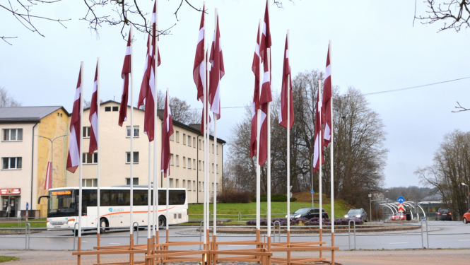 Latvijas karogu ornaments pie Valmieras apļa pilsētas centrā ar baltu autobusu fonā