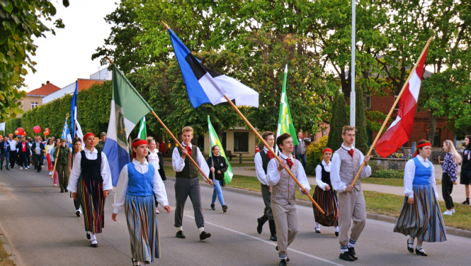 Jaunieši tautas tērpos gājienā ar latviešu un igauņu karogiem