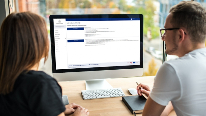 Vīrietis un sieviete sēž pie galda, skatās datora ekrānā un pilda gada ienākumu deklarāciju