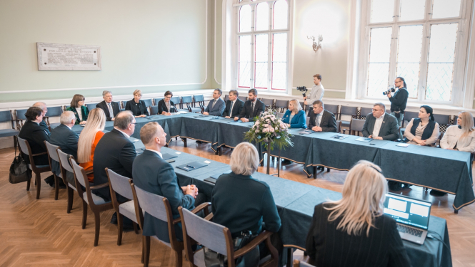 Cilvēki formālā apģērbā sēž pie U-formas galda