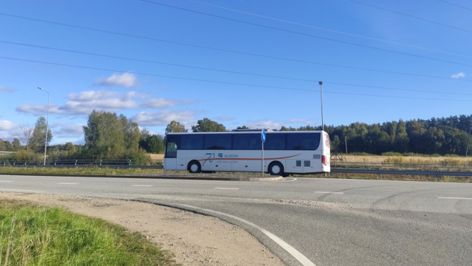 Balts autobuss uz ceļa, fonā zilas debesis