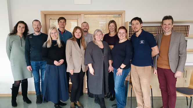 Dažādu profesionāļu grupas kopbilde gaišā, modernā biroja telpā. 