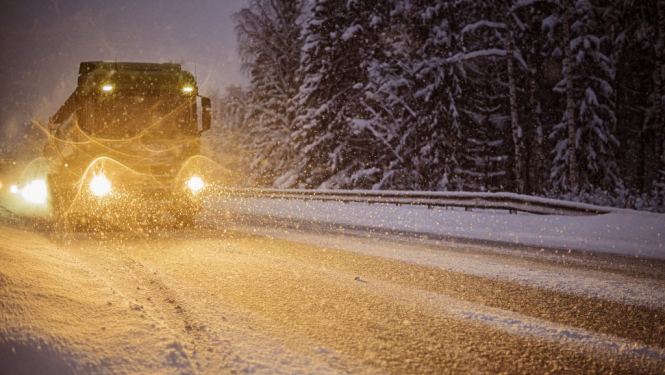 Smagais kravas auto uz sniegota ceļa tumšajā diennakts laikā