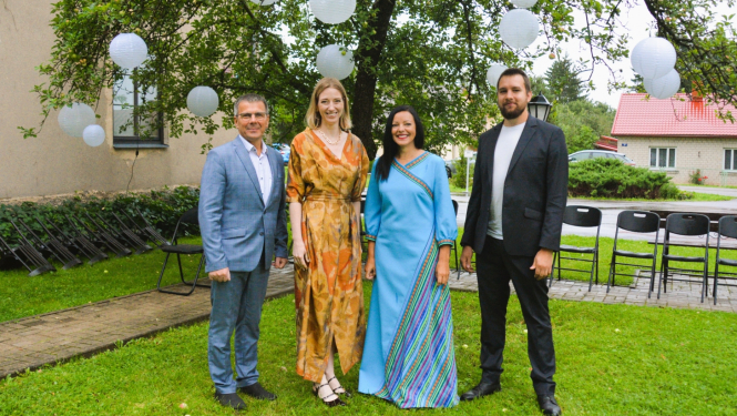 Divi vīrieši uzvalkos un divas sievietes kleitās muzeja pagalmā pie koka ar balonu dekorācijām