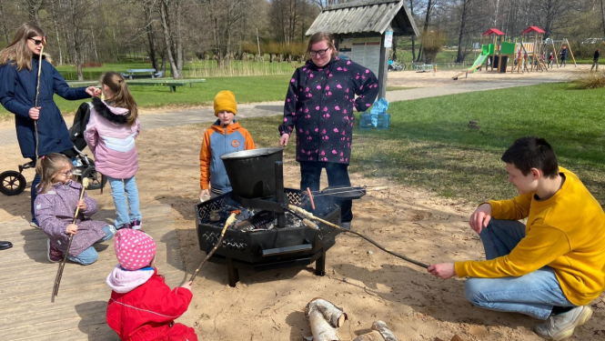 Ģimes ap ugunskura vietu cep desas