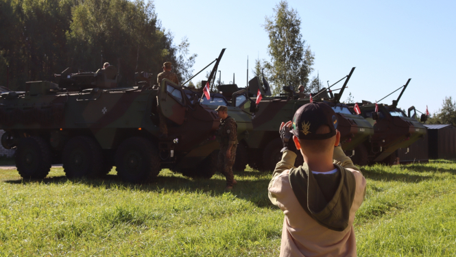 Zēns ar telefonu fotogrāfē rindā sastājušos bruņu transportierus