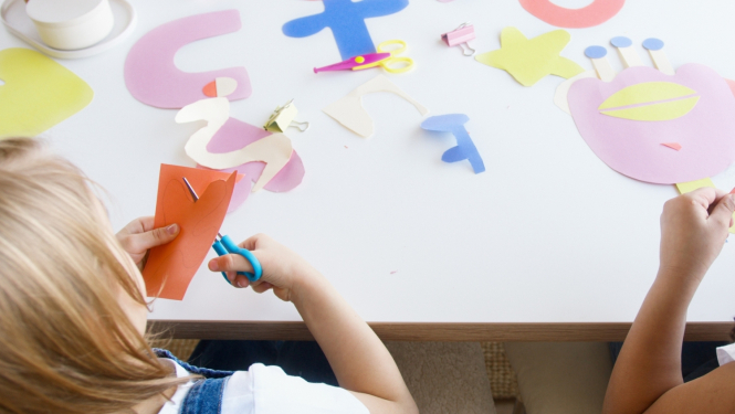 Bērns ar šķērēm griež krāsainu papīru