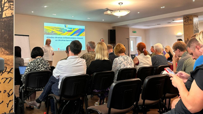 Cilvēki sēž krēslos un klausās lekciju