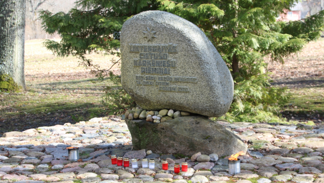 Piemiņas akmens Kārķos, kam apkārt saliktas sarkanbaltsarkanas piemiņas svecītes.