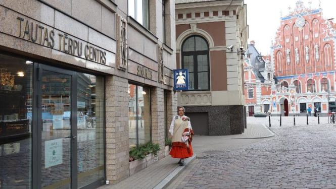 Sieviete latviešu tautas tērpā pie tautas tērpu centra ieejas