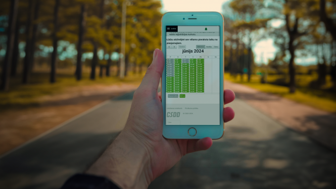 Cilvēka roka tur viedtālruni, kurā redzams pieraksta kalendārs