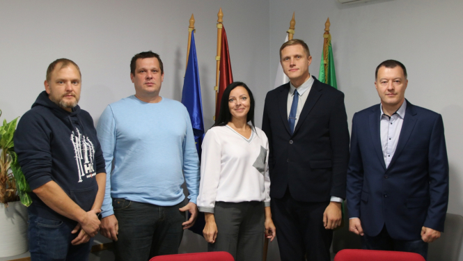 5 cilvēki pie karogiem apspriežu zālē