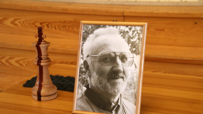 Vsevoloda Dudzinksa portretfotogrāfija blakus no koka izgrebtai šaha figūrai