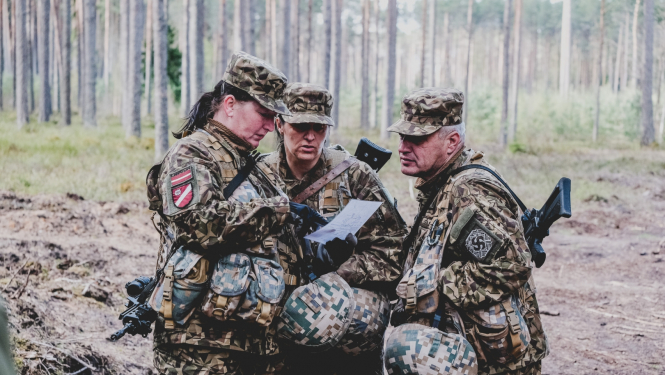 Trīs zemessargi formasterpos meža vidū pēta karti
