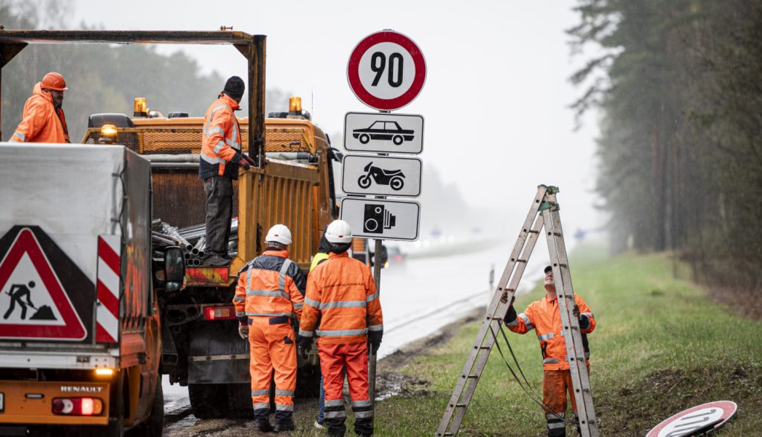 Ceļa strādnieki oranžos tērpos liek ceļa zīmes