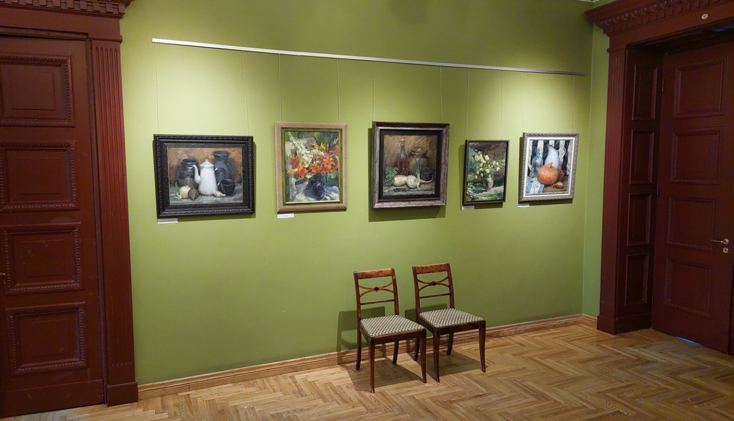 Gleznas uz zaļas sienas pie kuras ir divi krēsli