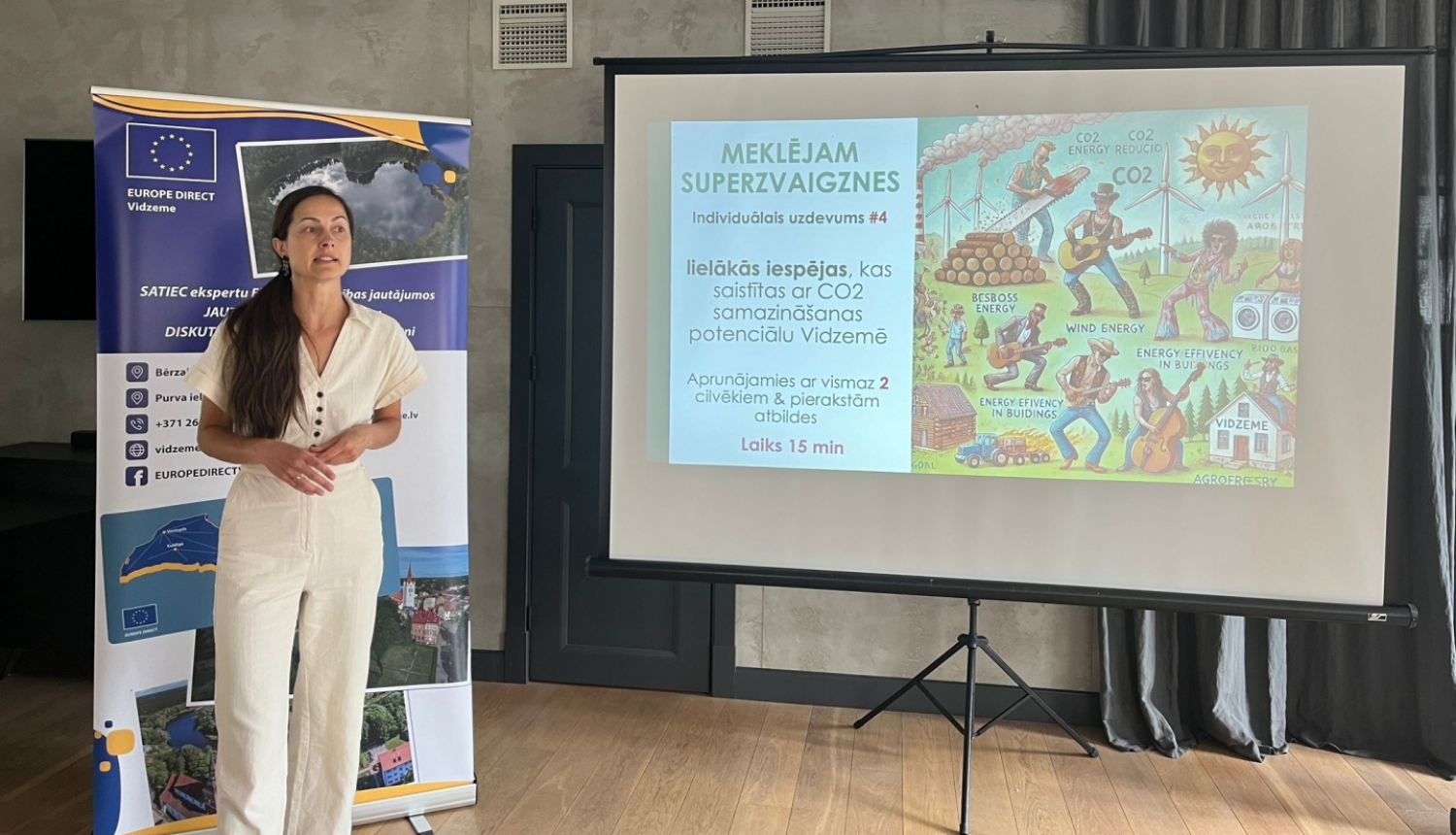 Sieviete ar tumšiem matiem balt\a kostīmā pie prezentācijas ekrāna