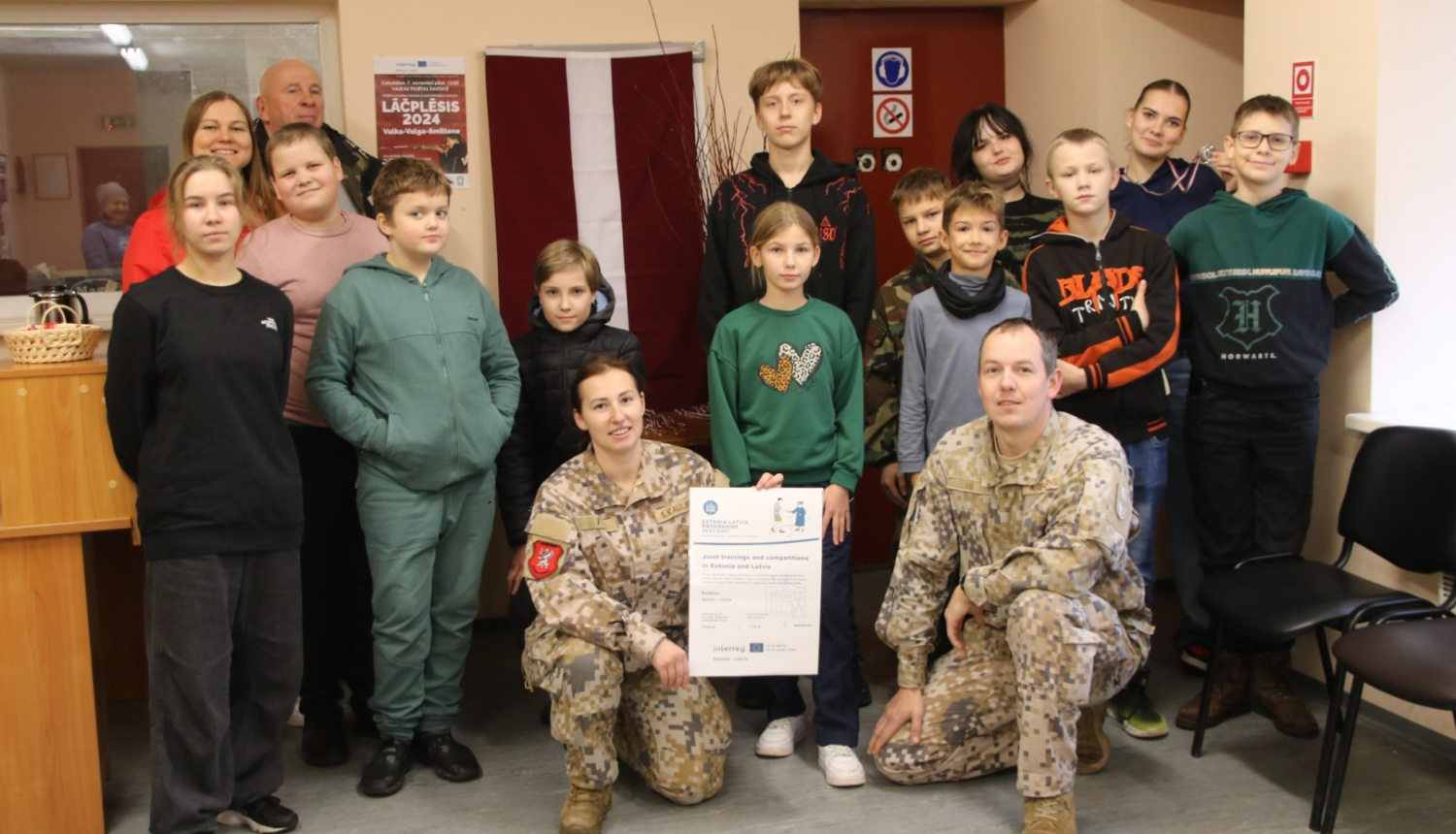 Sacensības dalībnieku un treneru kopbilde pie Latvijas karoga