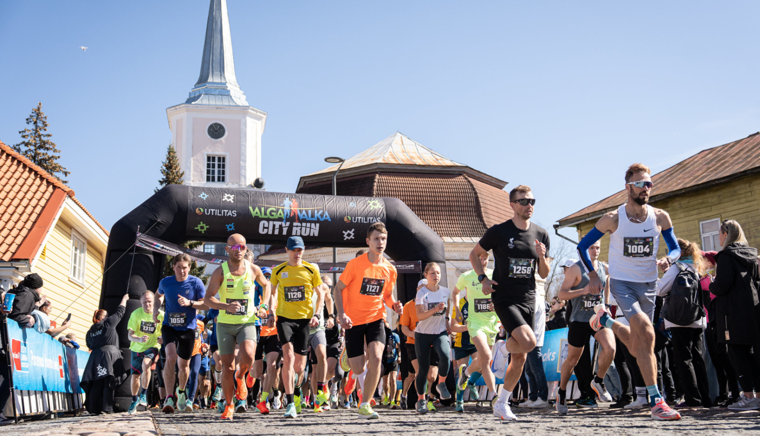 Skrējiena dalībnieki ar baznīcas torni fonā