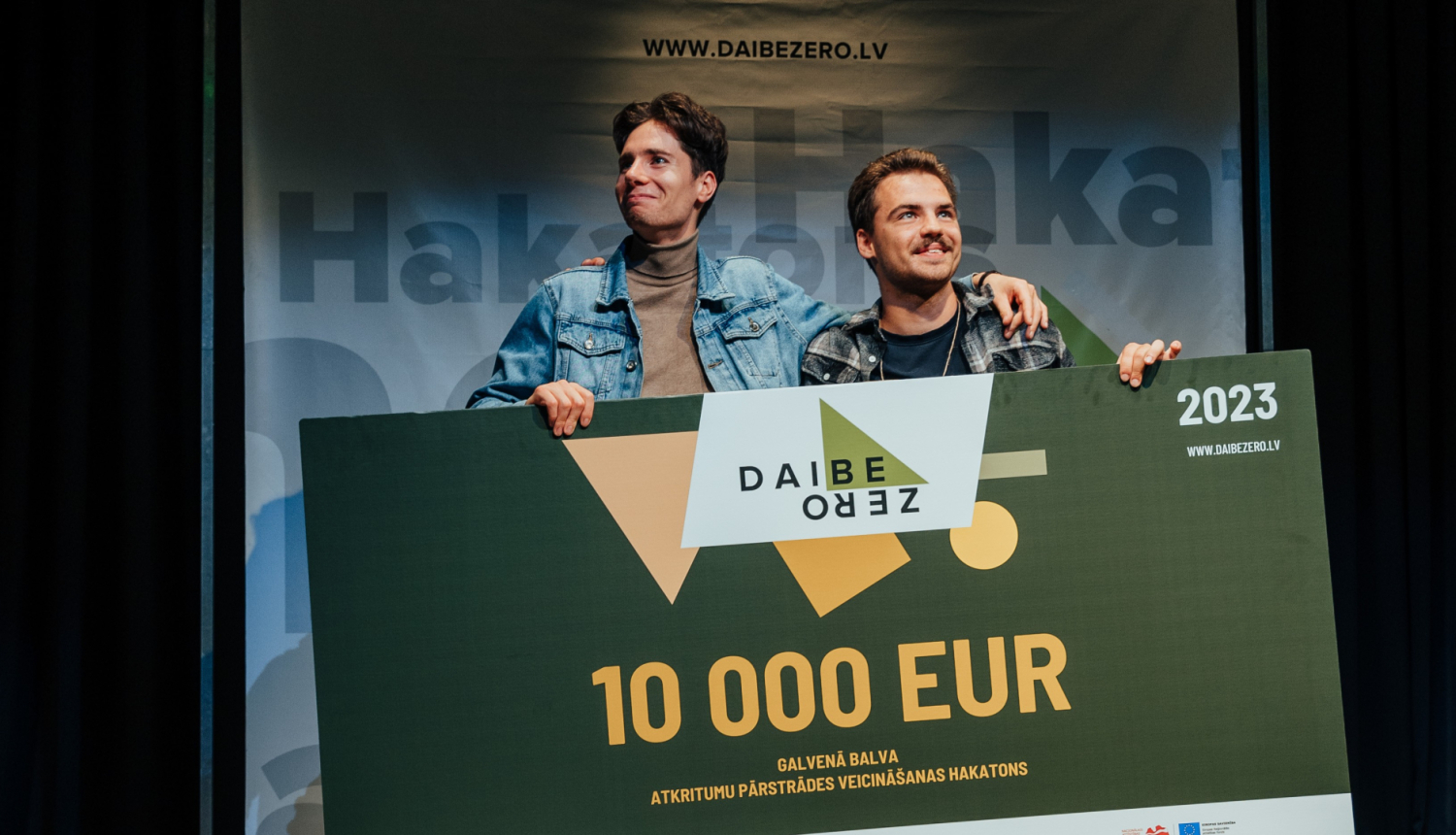 Smaidīgi vīrieši ar lielu baneri uz kā rakstīts 10 000 EUR